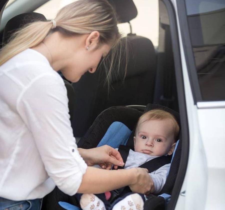 Mama troskliwie zapina pasy dziecku siedzącemu w foteliku samochodowym wewnątrz auta, dbając o jego bezpieczeństwo podczas podróży.